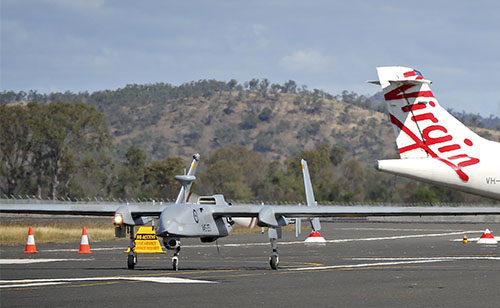 A Heron remotely piloted aircraft arrives at Rockhampton Airport in Queensland in front of a Virgin Australia civilian aircraft.