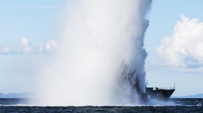 A plume of water dwarfs HMAS Diamantina as a high explosive charge is detonated to remove explosive remnants of war in the Solomon Islands. Photo by Corporal Steve Duncan.