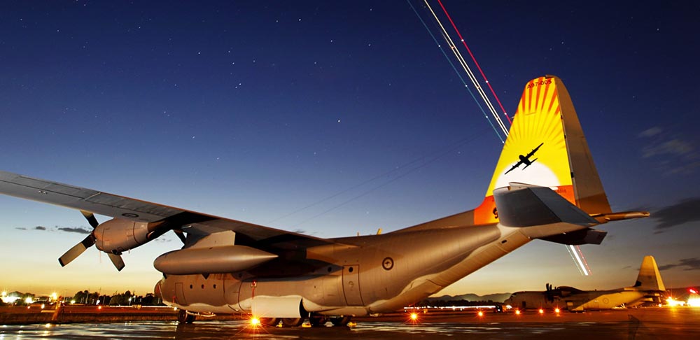 No. 37 Squadron C-130H Hercules A97-005 sports colourful tail art to to mark the type's retirement from Royal Australian Air Force service, on the RAAF Base Richmond flightline as a No. 34 Squadron Boeing Business Jet creates light trails in the sky. The tail art depicts a silhouette of a C-130H against a sunset, with the crests of No. 36 Squadron (Stallion) and No. 37 Squadron (Globe/Winged Water Carrier), representing the two units that had flown the C-130H. The RAAF operated a fleet of 12 C-130H Hercules from RAAF Base Richmond between 1978 until 2012. Photo by Corporal Amanda Campbell.
