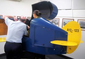 An Air Force Cadet receives instruction from an AAFC staff member before 'flying' Link Trainer A13-123.