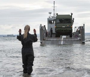 Greer Hutton of the anphibious beech team signals the driver of a MHOV to come forward off a landing craft. NZDF photo.