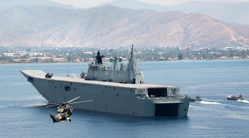 A MRH-90 Taipan helicopter delivers visitors from the Timor Leste government to HMAS Adelaide in Dili Harbour, as Navy and Army landing craft deliver a mobile hospital.