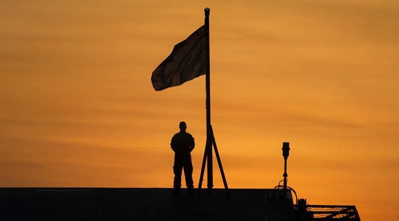 Signaller Aiden Barker prepares to lower the Australian National Flag at sunset on the Flight Deck of HMAS Adelaide while alongside Fort Hill Wharf, Darwin during Indo-Pacific Endeavour 17. Photo by Petty Officer Andrew Dakin.