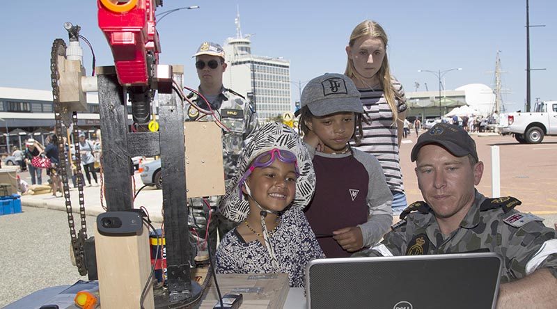 Petty Officer Chris White shows Akosua and Kk an auto targeting Nerf gun created for a robotics competition at the HMAS Stirling Fleet Support Unit-West display, during the Port of Fremantle Maritime Day held on Victoria Quay in Fremantle. Leading Seaman Bradley Darrell.