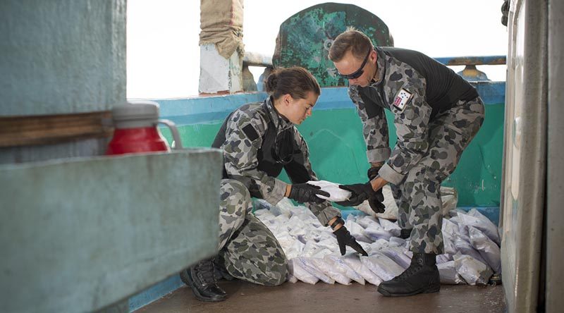 Able Seaman Stephanie Pannell passes a bag a seized narcotics to Leading Seaman James Walker during an illicit cargo seizure by HMAS Warramunga in the Middle East. Photo by Leading Seaman Tom Gibson.