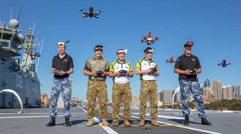 Drone racers, RAAF Officer Cadet Nicholas Eberl, Australian Army members Private Mackenzie Togo, Lieutenant Mark Sheppard and Lieutenant Thomas Gash, and RAAF Flight Sergeant Justin Galbraith, hover their drones over the flight deck of HMAS Canberra, to promote the inaugural Military International Drone Racing Tournament in the lead-up to Invictus Games. Photo by Able Seaman Leo Baumgartner.