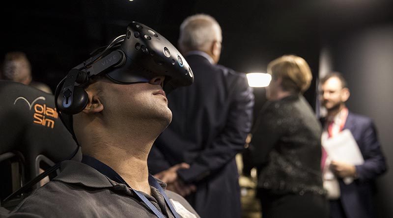 Vikas Nayak, Systems Integrator Lockheed Martin Australia, demonstrates Phase 1 of Joint Project 9711 Core Simulation Capability at Lockheed Martin Australia in Canberra, while VIP visitors chat in the background. Lockheed Martin photo.