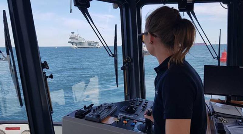 Australian tugmaster trainee Alicia Pollock at the helm of a Portsmouth, UK, tug, with HMS Queen Elizabeth inward bound. Photo by Rob Hinton @TugmasterRob