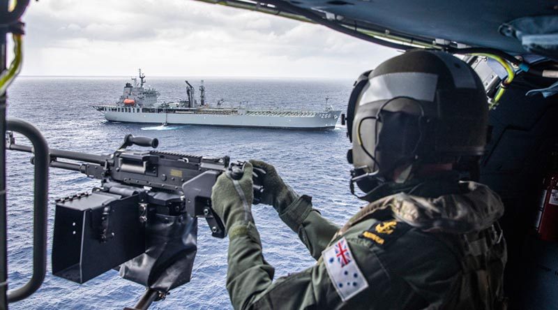 Leading Seaman Jason Griffiths mans the MAG 58 light support weapon in HMAS Stuart's MH-60R helicopter with HMAS Sirius in the background. Photo by Leading Seaman Tara Byrne.