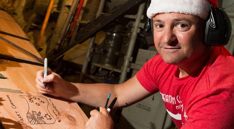 Flight Sergeant Geoff McLaughlin of Number 37 Squadron writes a message on an airdrop load destined for a Micronesian island during Operation Christmas Drop 2019. Photo by Corporal David Said.