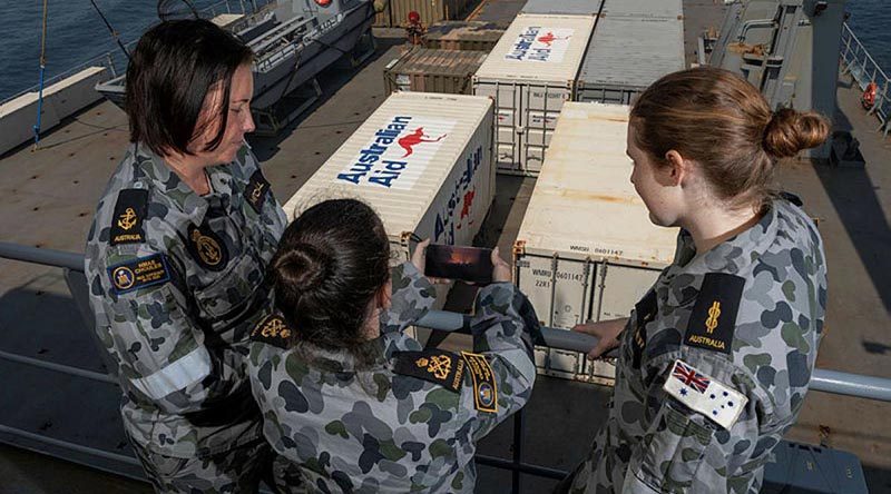 Petty Officer Helen Frank, centre, shows Leading Seaman Afton Mitchell, left, and Able Seaman Liliana Kleber a photo of how close the fire-front was to her parent's property in Orbost, Victoria. Photo: Leading Seaman Shane Cameron.