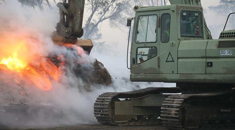 Australian Army engineers were swiftly redeployed 100km north from Cooma to Canberra in response to the Canberra fires on January 23rd. following a call from the ACT’s Emergency Services Agency. A bulldozer, excavator and grader were quickly loaded onto trucks and sent forward to the emergency zone. in this photo, Sapper Mathias Beddie, from the 2nd Combat Engineer Task Group – NSW, pulls-down piles of burning mulch so that bulldozers and graders can spread it for firefighters to douse with water. The piles are too dense to extinguish without first being spread and would otherwise smoulder for weeks and remain a fire hazard. Photo by Major Cameron Jamieson.