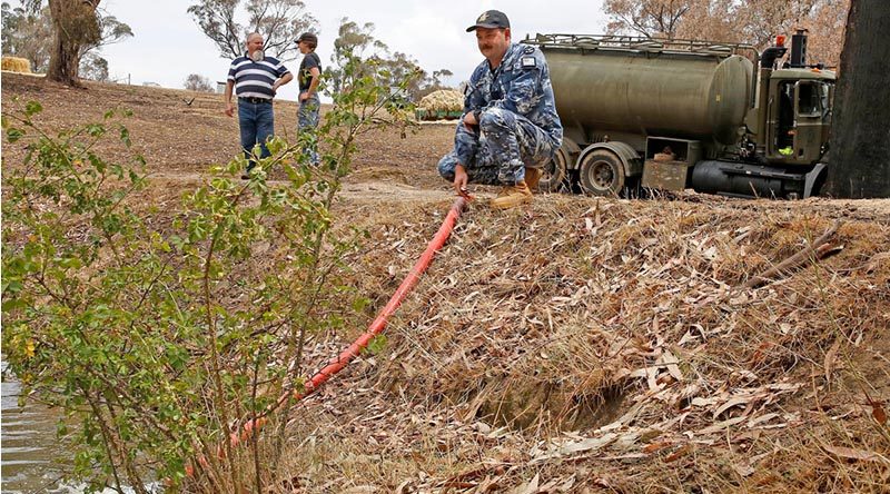 Air Force Leading Aircraftman Corrie Street, of No. 65 Squadron, RAAF Base Richmond, offloads 15,000 litres of much-needed water to farmer Rod Daisley of Tumbarumba, New South Wales, while Mr Daisley and Leading Aircraftwoman Tiane Westland, chat in the background. Photo by Sergeant Dave Morley.