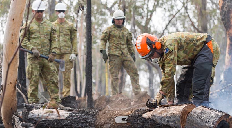 Australian Army Reserves Sapper Luke Willsmore from the 5th Engineer Regiment cuts a smouldering tree in an effort to prevent ongoing fires in the Jerangle region, NSW. Photo by Lance Corporal Brodie Cross.