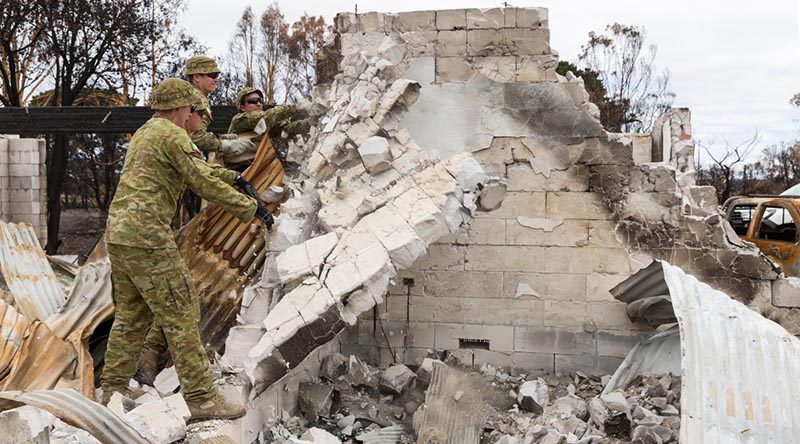 Soldiers from the 12th/40th Royal Tasmanian Regiment knock over a damaged wall of a home destroyed by bushfires on Kangaroo Island. Photo by Lance Corporal Brodie Cross.