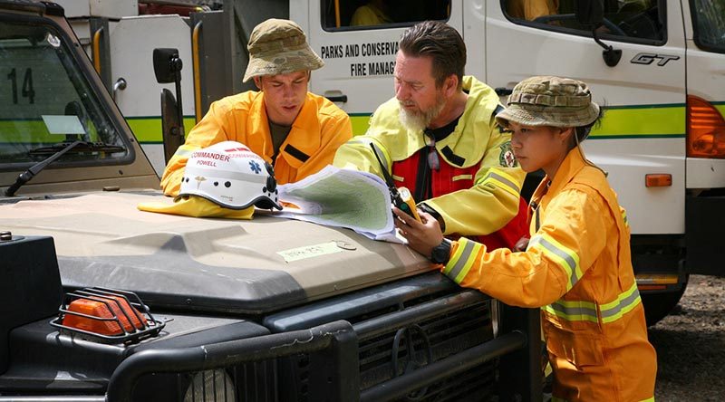 Ambulance Commander Joel Powell (centre), from the ACT Ambulance Service, discuss firefighting operations with Lance Corporal Matt Fegeleson, while Lance Corporal Jessica Zhang monitors emergency services radio traffic, in the Brindabella Ranges. Together they form a remote-area ambulance team, using a six-wheel drive Army G-Wagon ambulance, to support an ACT Rural Fire Service strike team operating in remote woodlands. Photo by Major Cameron Jamieson.