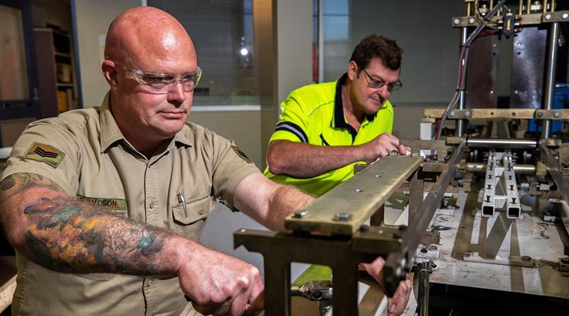 Australian Army soldier Sergeant Steven Davidson assists Bob Neighbour to repair a medical mask manufacturing machine at Med-Con Pty Ltd. Photo by Corporal Sagi Biderman.