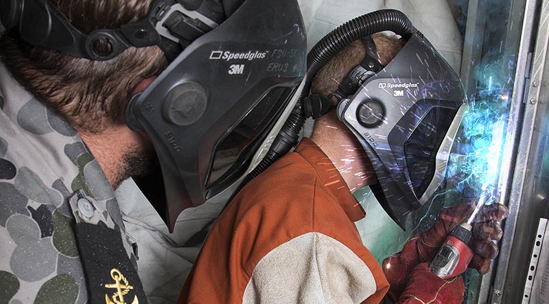 Royal Australian Navy sailor Leading Seaman Cameron Campbell supervises Able Seaman Matthew Gates in a welding task. Photo by Petty Officer James Whittle, digitally enhanced by CONTACT (adding extra weld sparkles).