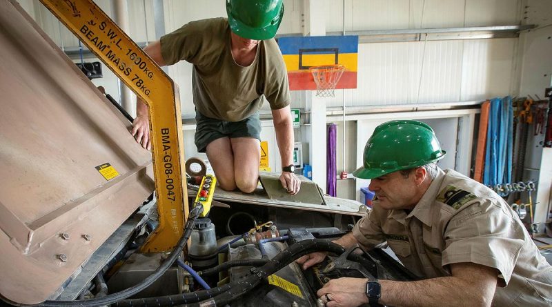 Lance Corporal Cameron Pennell, left, and Rear Admiral Michael Rothwell begin removing the engine from a protected mobility vehicle in the Middle East region. Photo by Sergeant Ben Dempster.