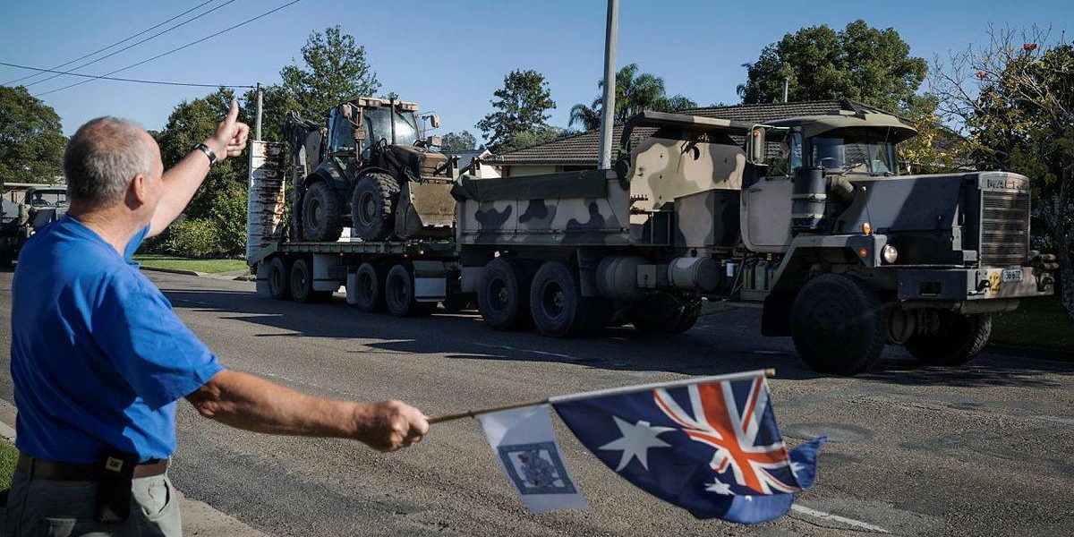 Darcy Elbourne waves the Australian flag in the driveway of his home as Army personnel head out to conduct relief and recovery tasks during Operation NSW Flood Assist in Taree. Photo by Corporal Sagi Biderman.