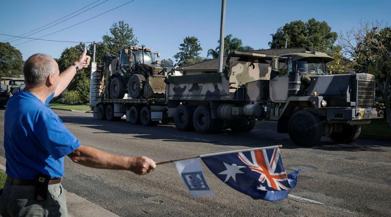 Darcy Elbourne waves the Australian flag in the driveway of his home as Army personnel head out to conduct relief and recovery tasks during Operation NSW Flood Assist in Taree. Photo by Corporal Sagi Biderman.