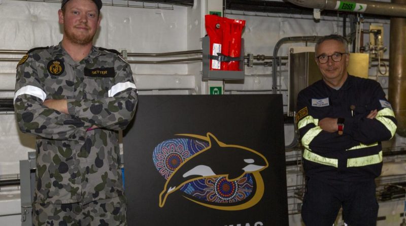 Leading Seaman Jackson Setter, left and Navantia Australia engineer Jose Luis Bouza Fernandez stand with a new passageway sign for HMAS Supply. Story by Lieutenant Jessica Craig. Photo by Able Seaman Benjamin Ricketts.