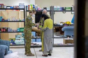 Corporal Nikkiska McGlashan from 3 Combat Signal Regiment, assists an evacuee to gather essentials at a temporary camp, in Australia’s main operating base in the Middle East. Photo by Leading AircraftWoman Jacqueline Forrester.