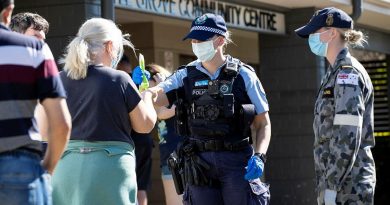 NSW Police Constable Megan Green and Seaman Jordan Parsons hand out sunscreen to civilians waiting in line for a COVID-19 test at the Wattle Grove Community Centre. Story by Lieutenant Commander John Thompson. Photo by Corporal Dustin Anderson.