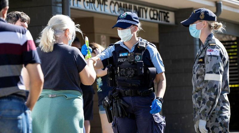NSW Police Constable Megan Green and Seaman Jordan Parsons hand out sunscreen to civilians waiting in line for a COVID-19 test at the Wattle Grove Community Centre. Story by Lieutenant Commander John Thompson. Photo by Corporal Dustin Anderson.
