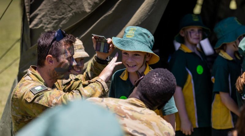 Soldiers from the 7th Combat Signal Regiment apply camouflage cream to a student at Gympie East State School. Story by Captain Jesse Robilliard . Photo by Patrick Maher.