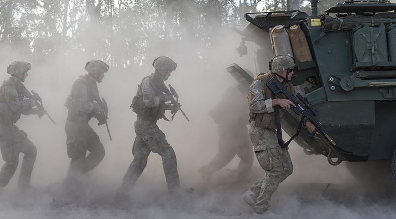 New Zealand Army infantry 'indian file' behind a moving Light Armoured Vehicle. NZDF file photo.