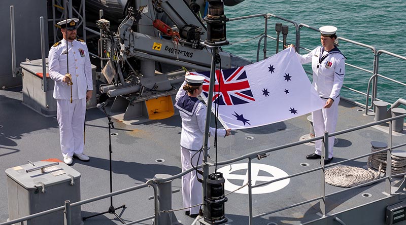 Commanding Officer HMAS Glenelg Lieutenant Commander Alexander Finnis stands at attention as Leading Seaman Kiani Hughes and Able Seaman Eliza McGuigan strike the Australian White Ensign for the final time during the ships' decommissioning ceremony at HMAS Coonawarra, Darwin. Photo by Leading Seaman Shane Cameron.