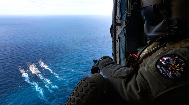 Leading Seaman Nathan Cox watches out of HMAS Arunta's embarked MH-60R helicopter "Athena" as HMAS Arunta (right) and USS Milius conduct a duel Replenishment at Sea with JS Oumi during Exercise Malabar 2022. Photo by Leading Seaman Susan Mossop.