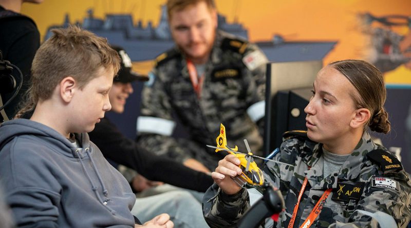 Able Seaman Aviation Technician – Aircraft Casey Anderson assists a member of the public with a Royal Australian Navy Fleet Air Arm flight simulator inside the RAN exhibition tent the 2023 Avalon International Airshow. Story by Lieutenant Ben Willee. Photo by Corporal David Cotton.