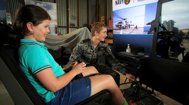 Seaman Liam Cox, from HMAS Albatross, guides eight-year-old Kira on the Navy helicopter simulator display at the Hunter Valley Airshow. Story by Flight Lieutenant Thomas McCoy. Photo by Sergeant Glen McCarthy.