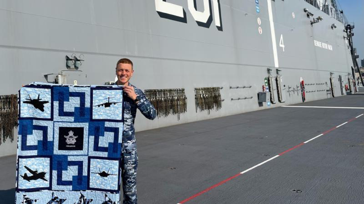 Flight Lieutenant Kristian Henderson proudly displays his Aussie Hero Quilt, received while deployed with HMAS Adelaide on Operation Tonga Assist 22. Story by Squadron Leader Jessica Aldred.