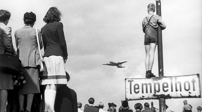 Berlin civilians watch an airlift plane land at Templehof Airport, 1948. United States Air Force Historical Research Agency photo, via Wikipedia.