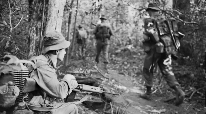 Vietnam. 1966-11-28. Private Ken Wallace of Mitchelton, Brisbane, Qld, keeps a sharp watch as his mates in the 6th Battalion, The Royal Australian Regiment (6RAR), advance along a jungle track during Operation Ingham. Australian War Memorial file number CUN/66/0932/VN