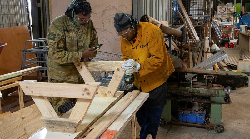 Private Luke Kennedy assists a fellow Amata community member with the construction of a bench seat. Story by Major Evita Ryan. Photo by Private Jack Hayes.